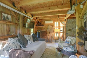 A cozy cabin interior with a bed, a wooden dresser, and a dining table. - Fire Pit, Deck! Rural Retreat Near East Beach (Charlestown)
