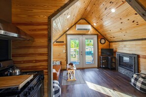 A cozy cabin interior with a kitchen, a fireplace, and a living area with a television. - Communal Fire Pit & Dock! Tiny Home By Lake Murray (Gilbert)