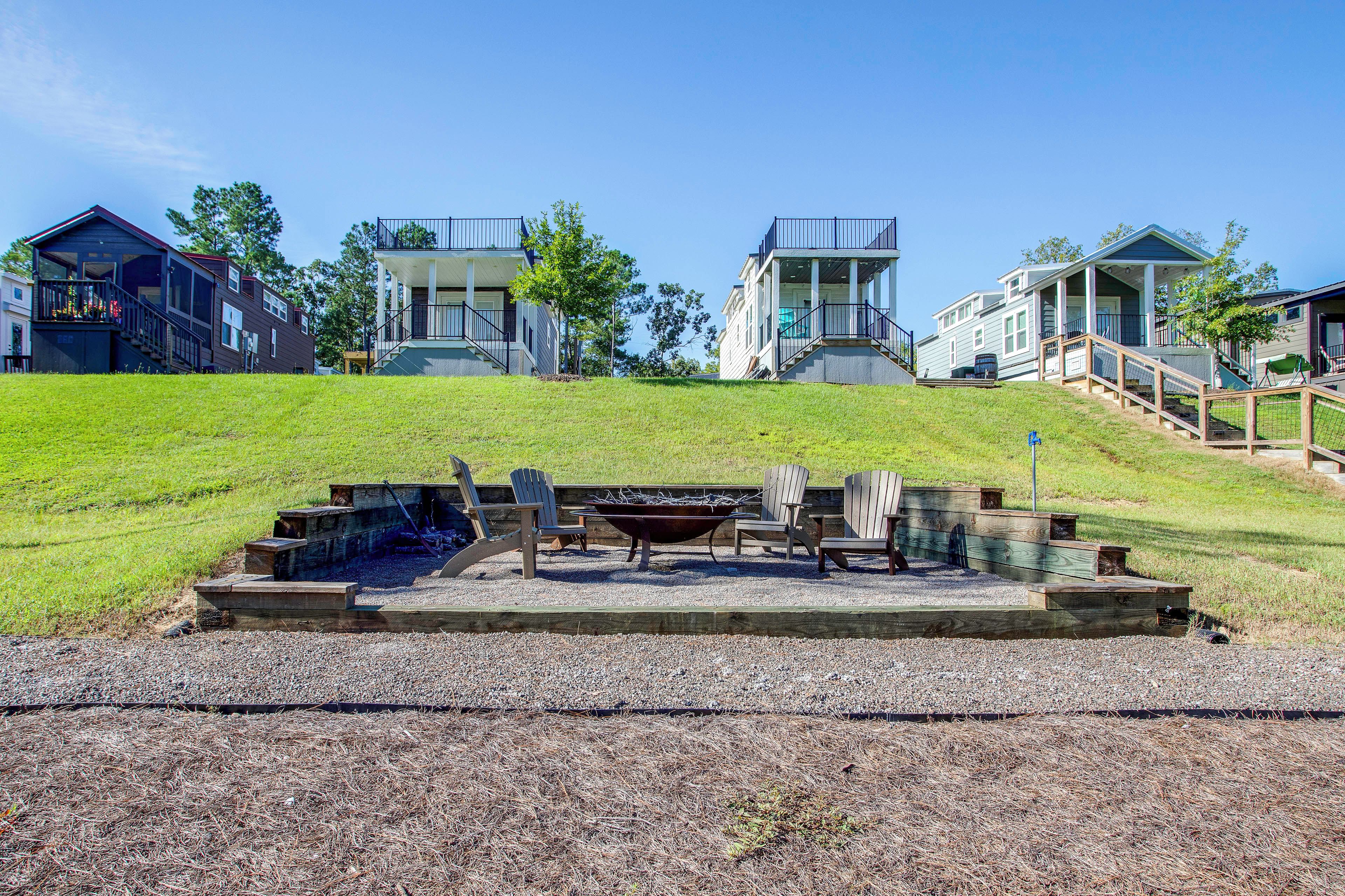 A residential area with houses on a grassy hill, outdoor seating, and a fire pit.