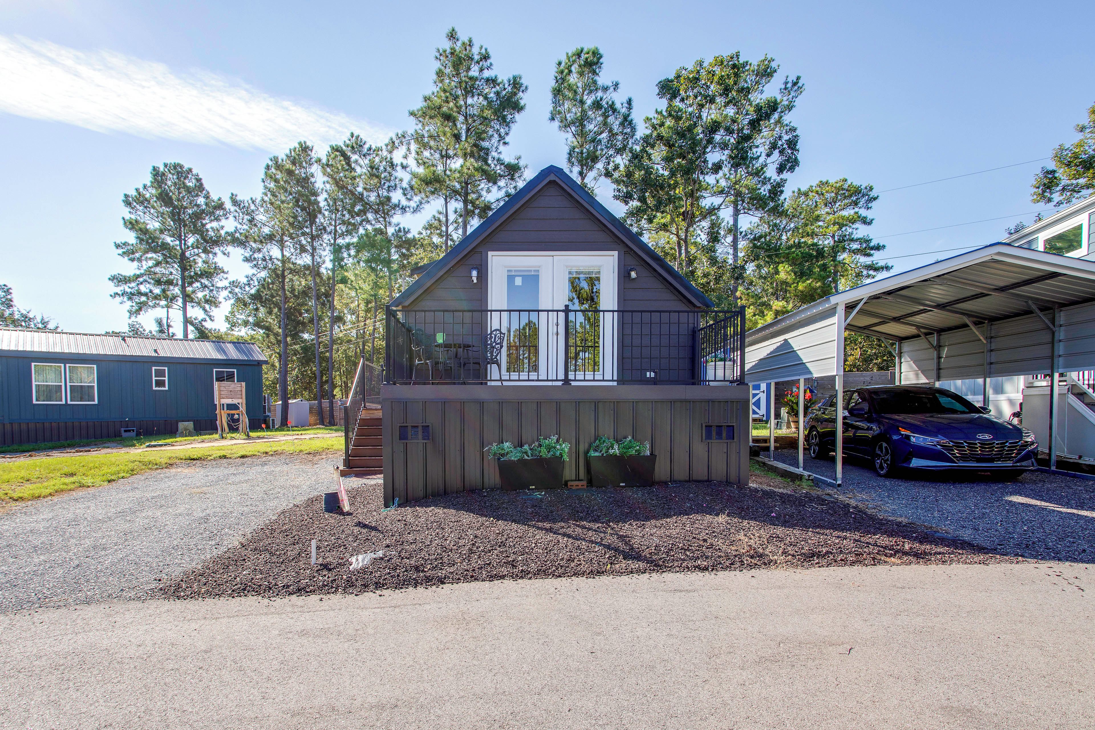 A two-story cabin with a front porch, a covered garage, and a gravel driveway.