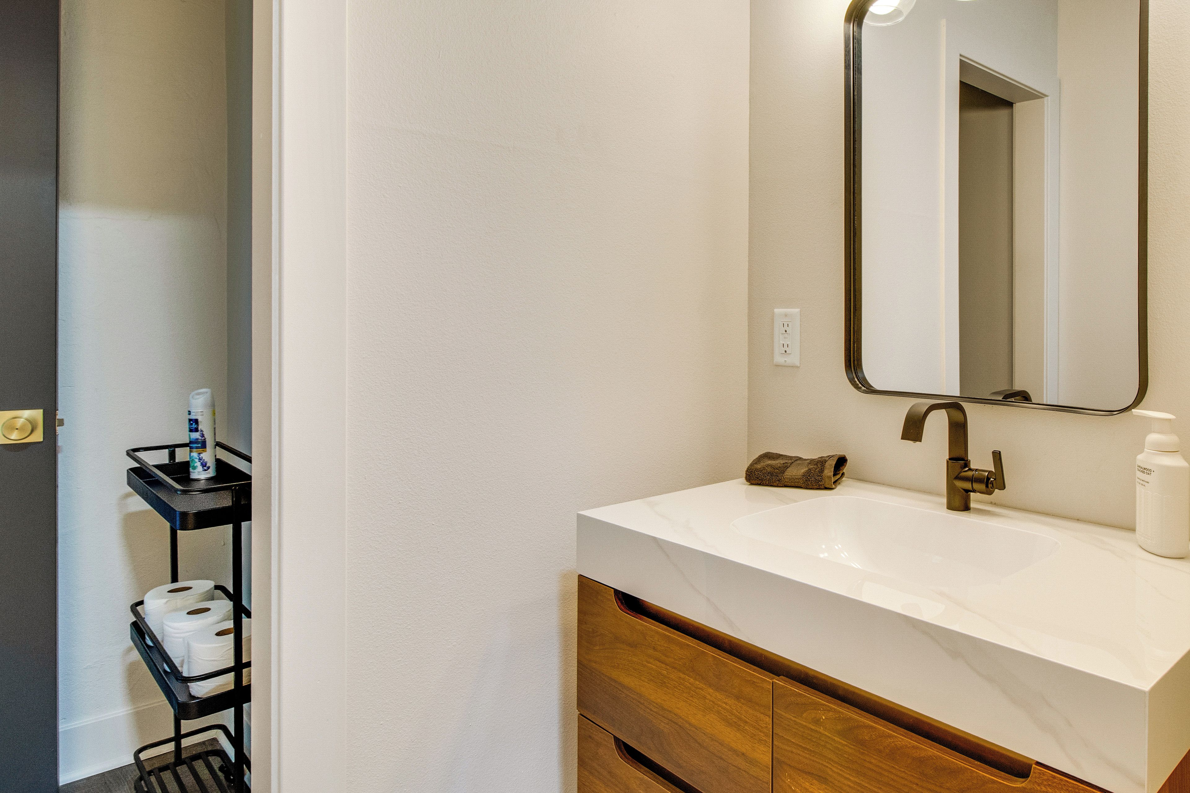 A bathroom with a white sink, a mirror, a towel, and a bottle of shampoo.