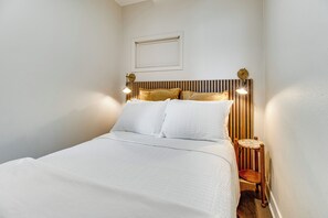 Una cama bien hecha con ropa de cama blanca en una habitación con cabecera de madera y una pequeña silla de madera.