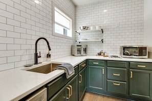 A kitchen with white subway tiles, a stainless steel sink, a microwave, and green cabinets. - Remodeled Getaway in the Heart of Mountain Home! (Mountain Home)