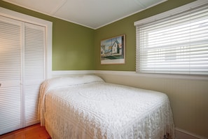 Ein Schlafzimmer mit einem Einzelbett, einem Gemälde an der Wand und einem Fenster mit Jalousien.