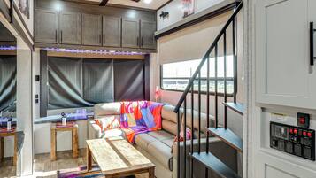 A compact RV interior with a kitchenette, a dining area, a sofa with a colorful blanket, and a staircase.