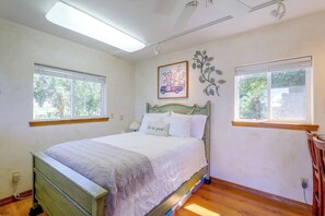 Un dormitorio con cama, dos ventanas, un cuadro colgado en la pared y un radiador.