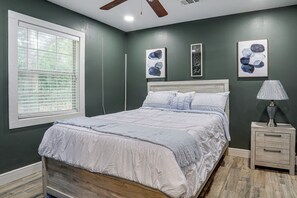 Un dormitorio con cama, mesita de noche, lámpara y obras de arte en las paredes.