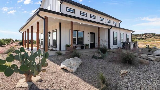 A two-story house with a covered porch, large windows, and a desert landscape. - Private Pickleball Court! Family Glen Rose Getaway (Glen Rose)