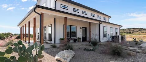 A two-story house with a covered porch, large windows, and a desert landscape.