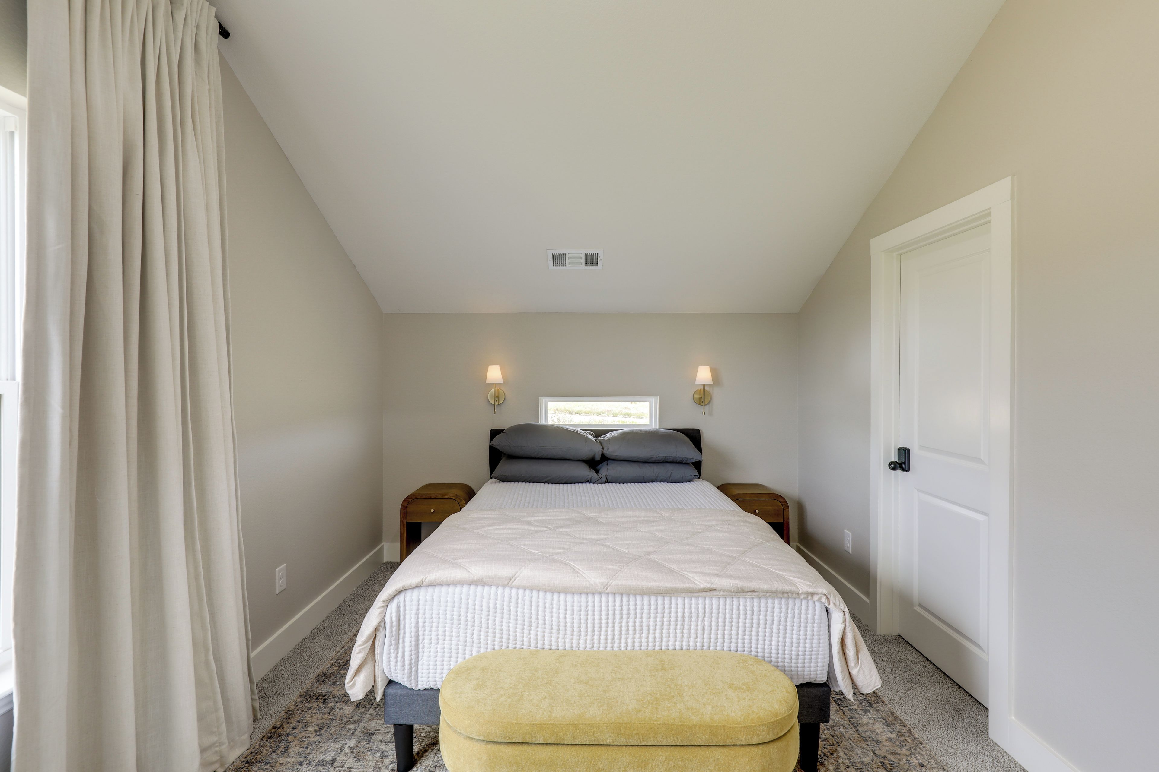 A bedroom with a bed, two bedside tables, a window, a door, and a curtain.