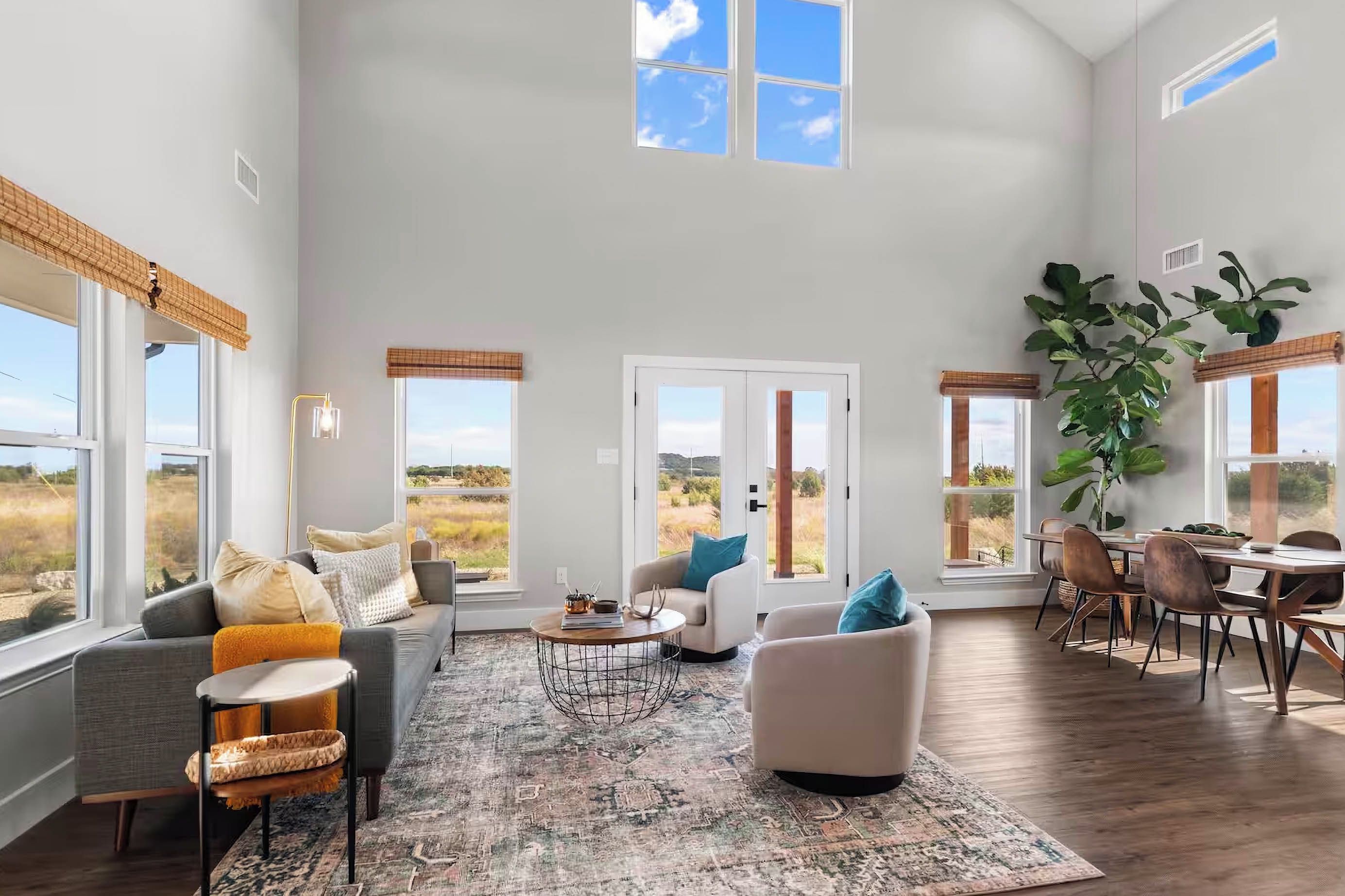 A spacious living room with a high ceiling, large windows, and a view of the outdoors.