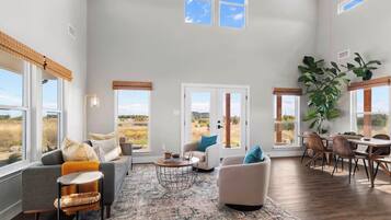A spacious living room with a high ceiling, large windows, and a view of the outdoors.