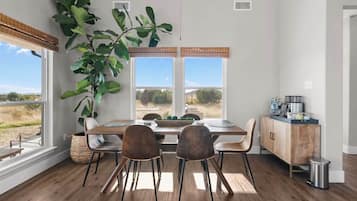 A dining area with a wooden table, four chairs, a large potted plant, and a view of the outdoors through a window.
