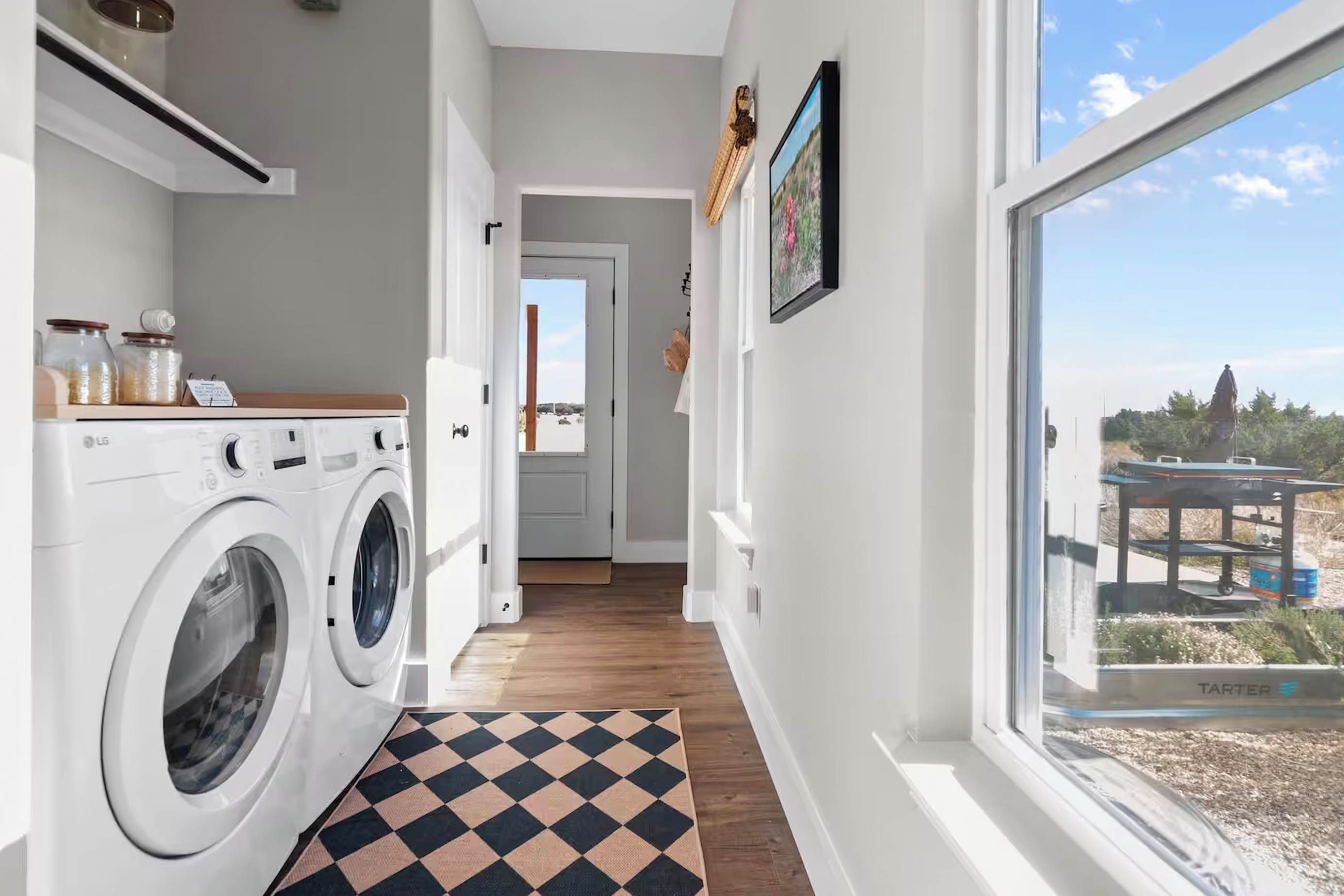 A laundry area with a washing machine, a checkered mat, and a window with a view of the outdoors.