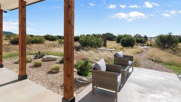 A covered patio with outdoor furniture, a concrete floor, and a view of a natural landscape with shrubs and trees.