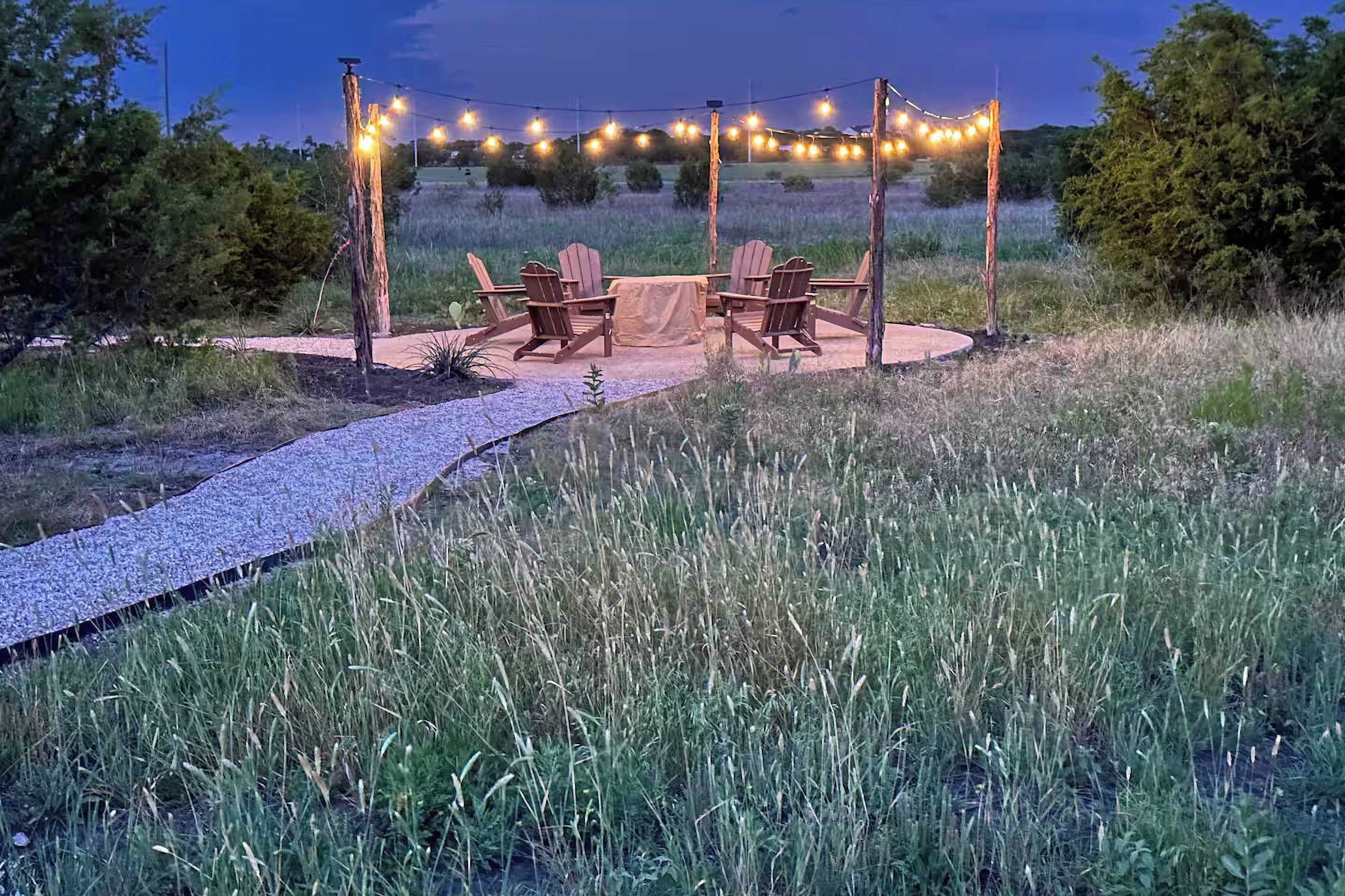 An outdoor seating area with wooden chairs and a table, surrounded by a gravel path and string lights.