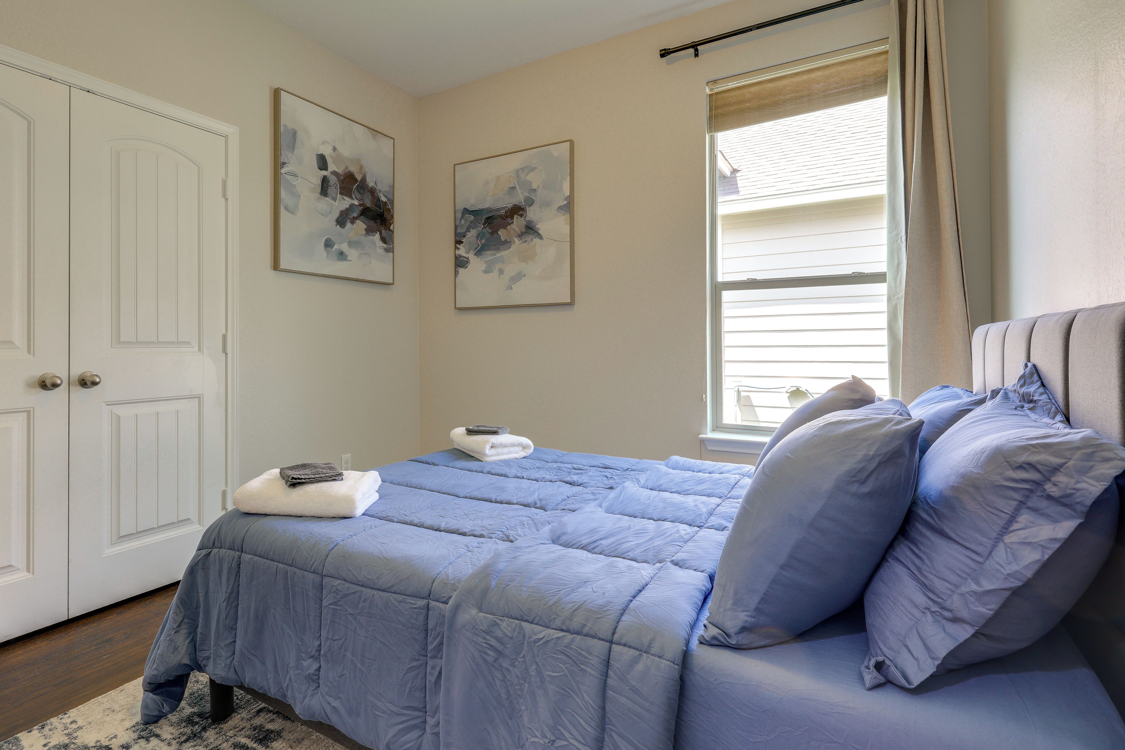Un dormitorio con cama, una ventana con persianas y dos cuadros abstractos en la pared.