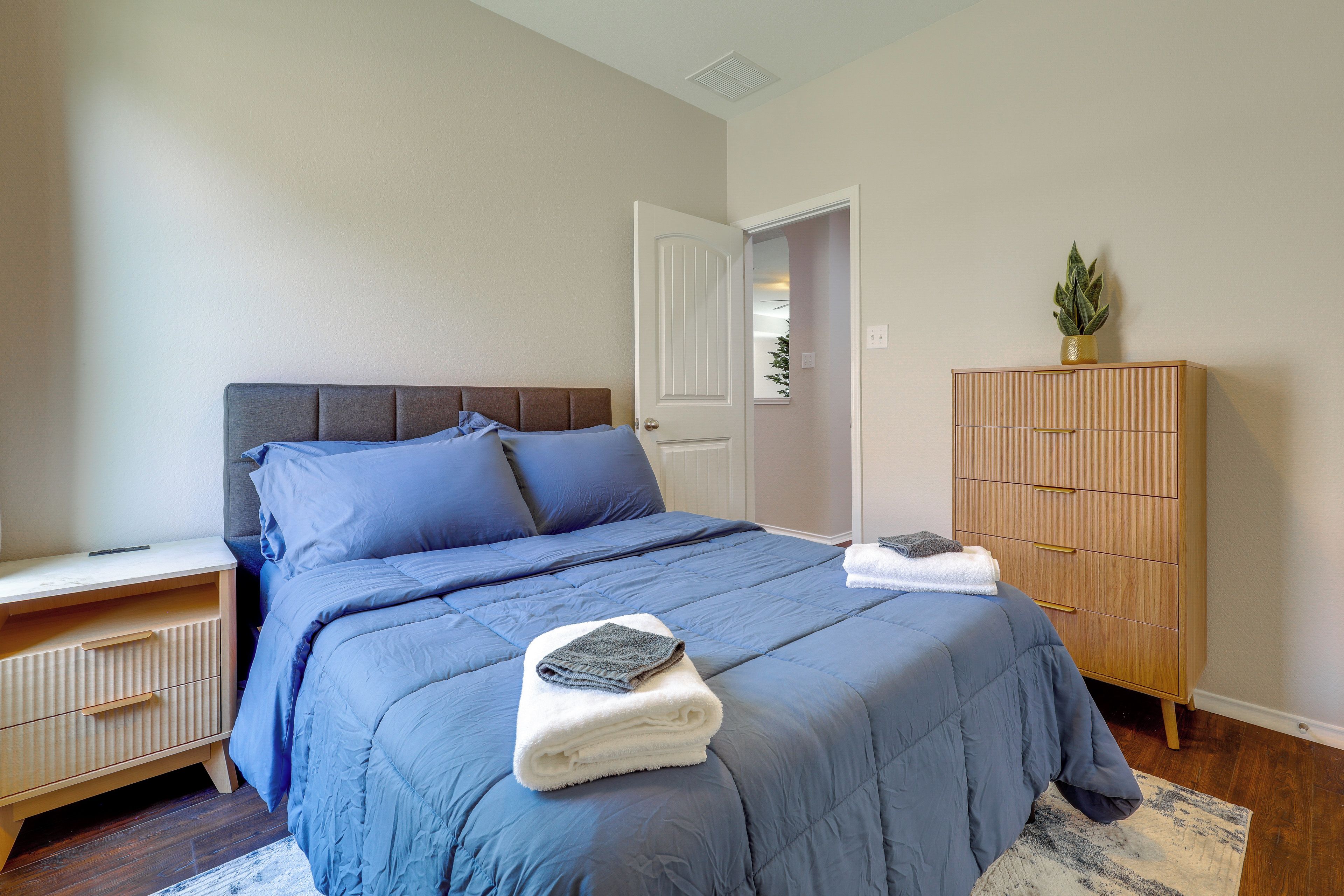 Une chambre à coucher avec un lit, une table de chevet, une commode en bois et une plante en pot.