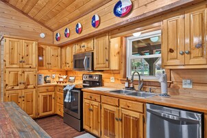 Una cocina con gabinetes de madera, un microondas de acero inoxidable, un horno, un lavavajillas y una ventana con vistas al exterior.