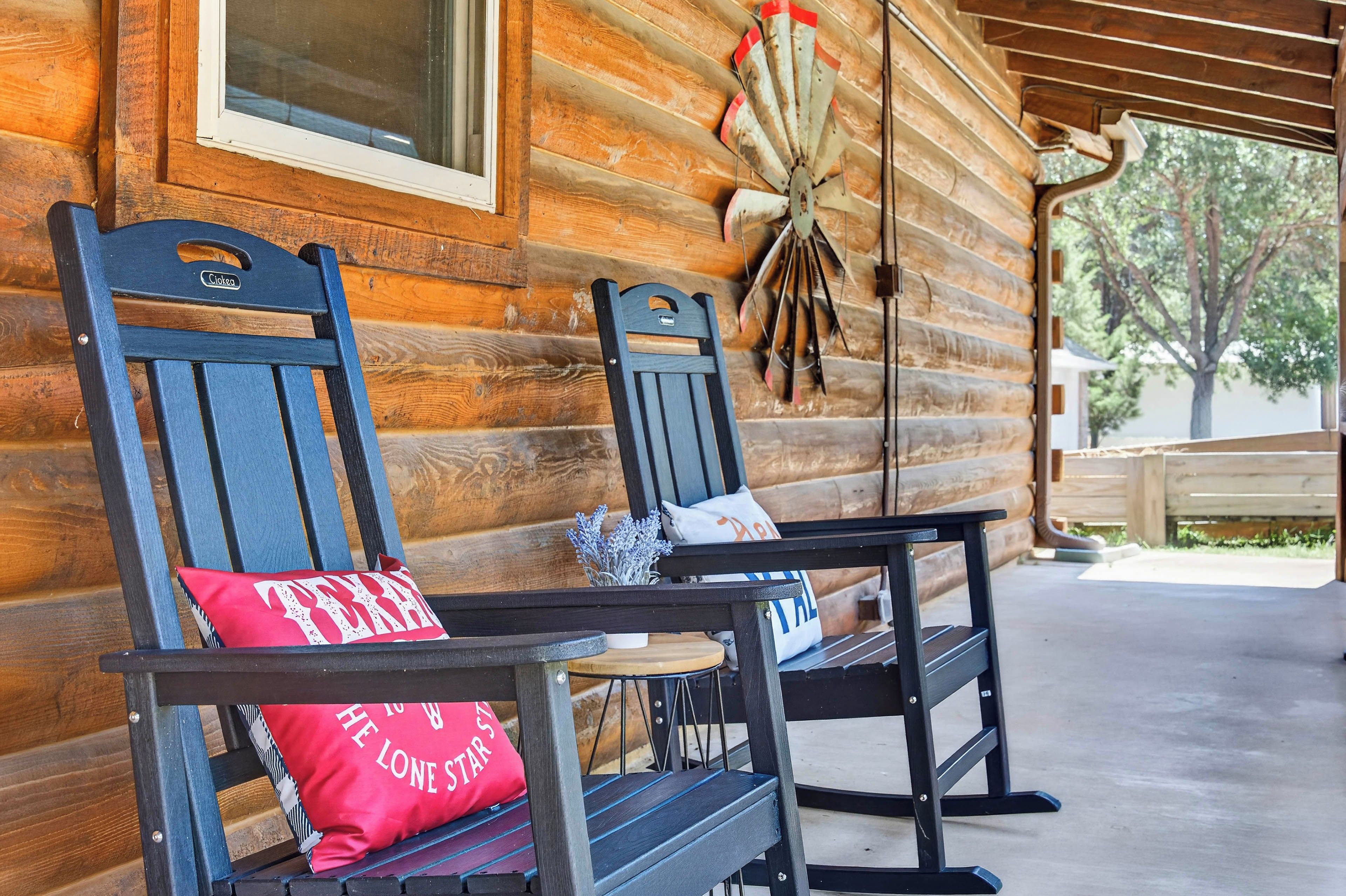 Two wooden chairs with cushions on a porch of a log cabin.
