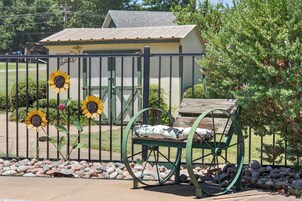 Un jardín cercado con un banco, un cobertizo pequeño y una fila de girasoles.