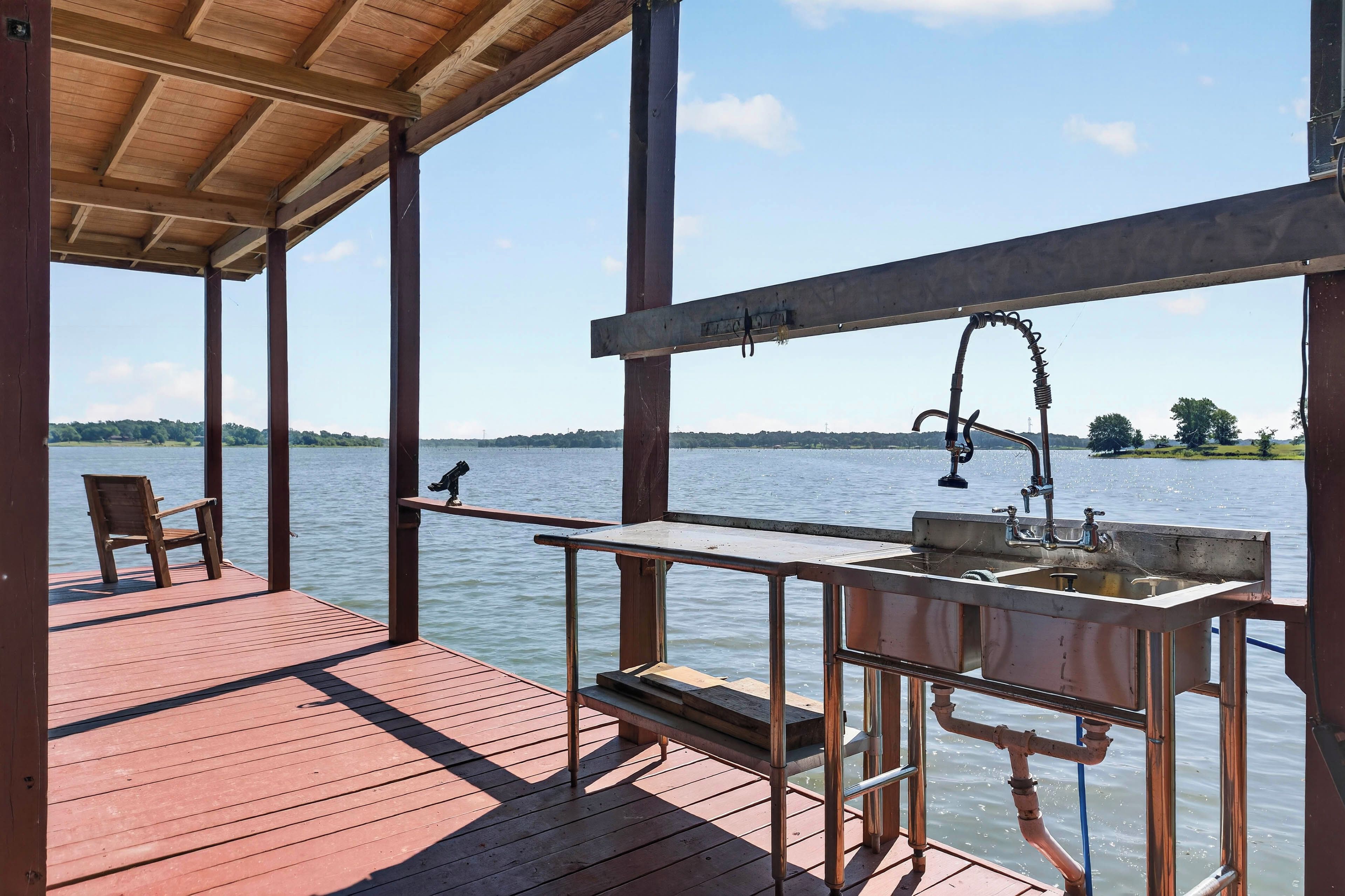 Une terrasse en bois avec une rambarde en métal donnant sur une étendue d’eau, un banc et un évier en métal.