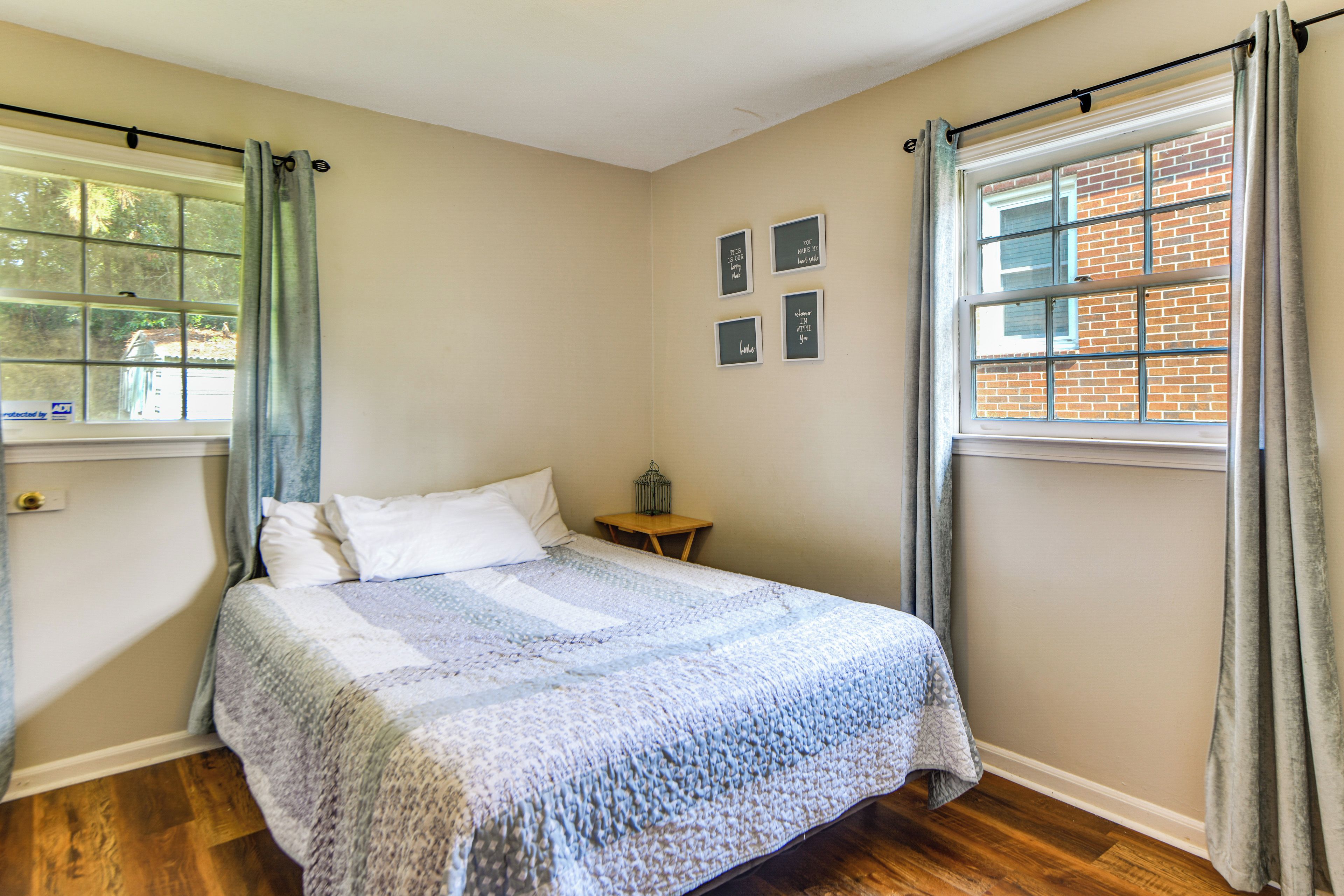 A bedroom with a bed, a nightstand, a window with curtains, and a wall with framed pictures.