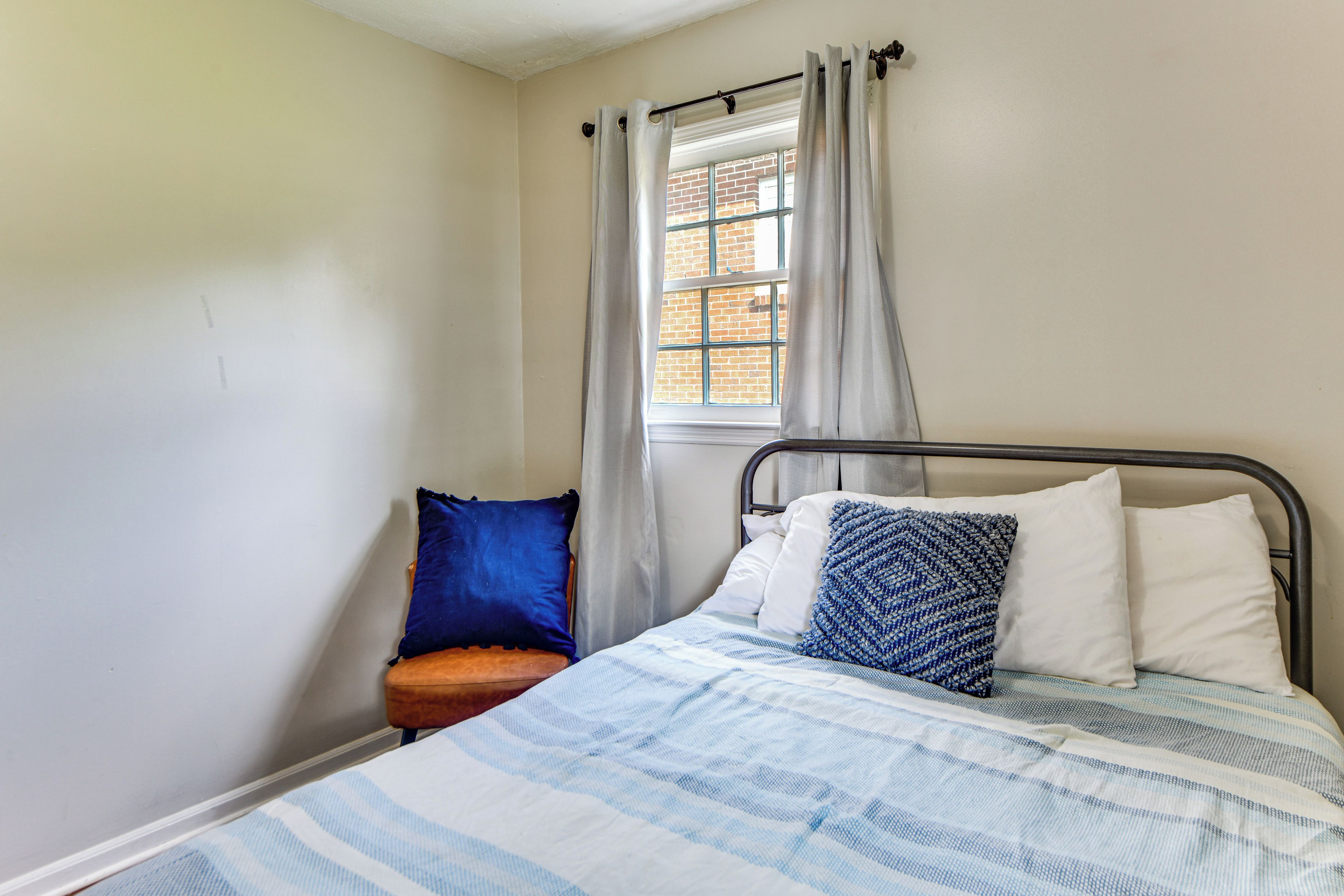 A single bed with a metal frame, a window with curtains, and a chair with a cushion.