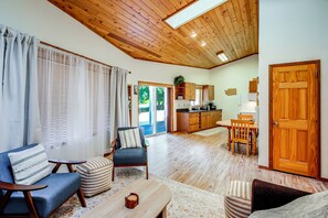 Un amplio espacio habitable con techo alto, piso de madera, una mesa de comedor y una cocina al fondo.