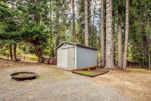A small, single-story shed with a door and a window, surrounded by a gravel area and a metal fire pit.