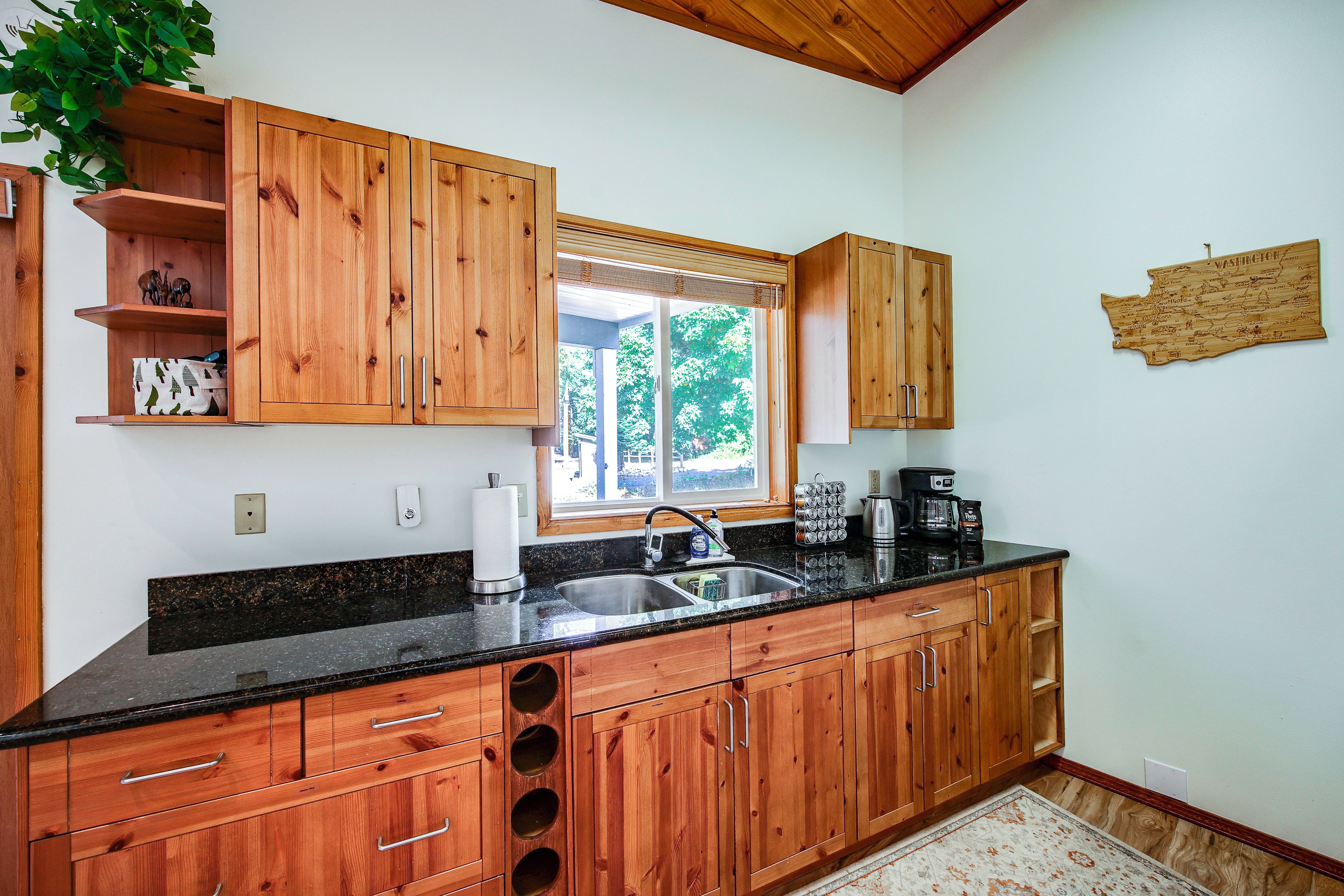 A kitchen with wooden cabinets, a black countertop, a window with blinds, and a map on the wall.