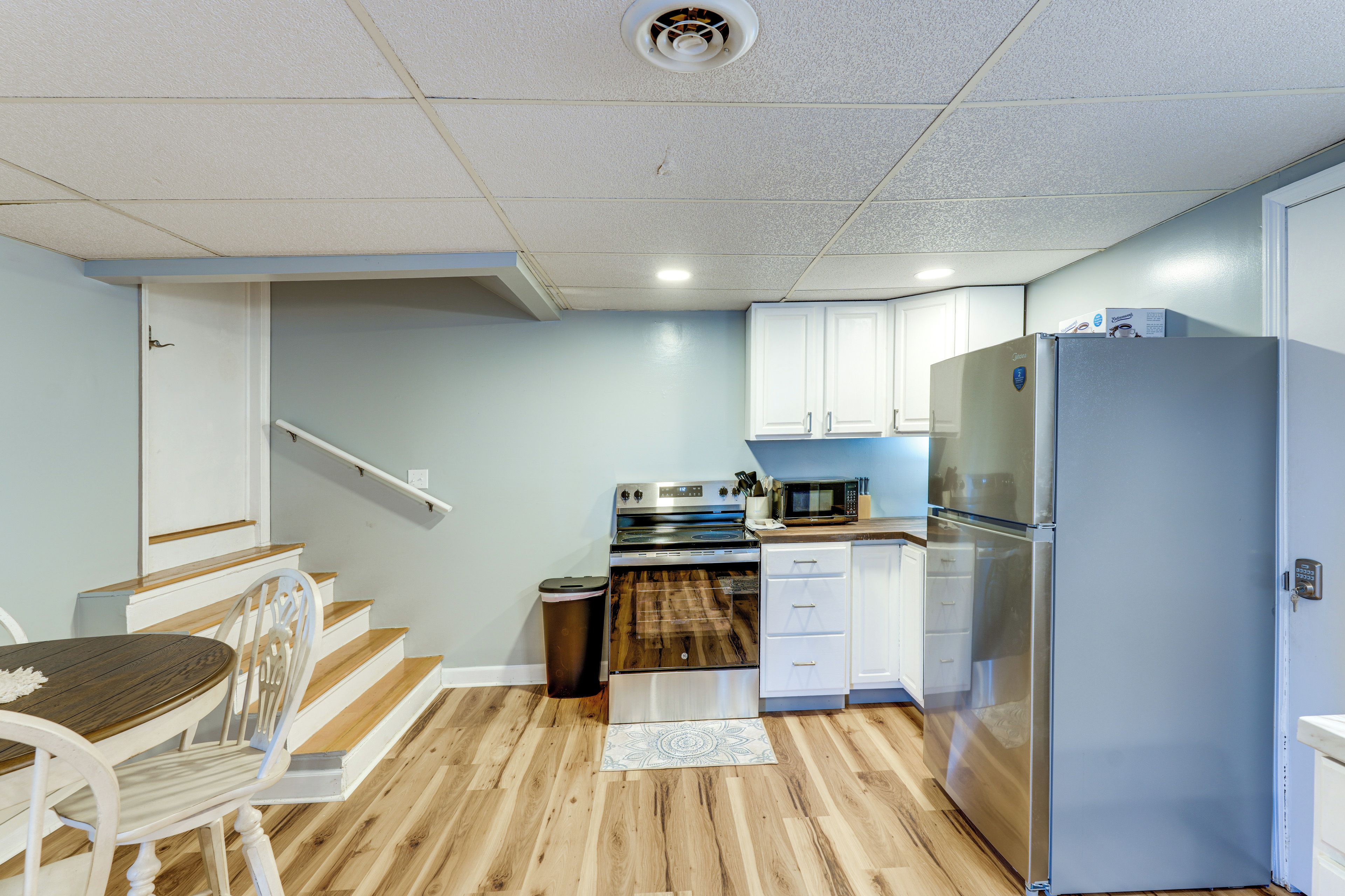 A compact kitchen with white cabinets, a stainless steel refrigerator, and a microwave.