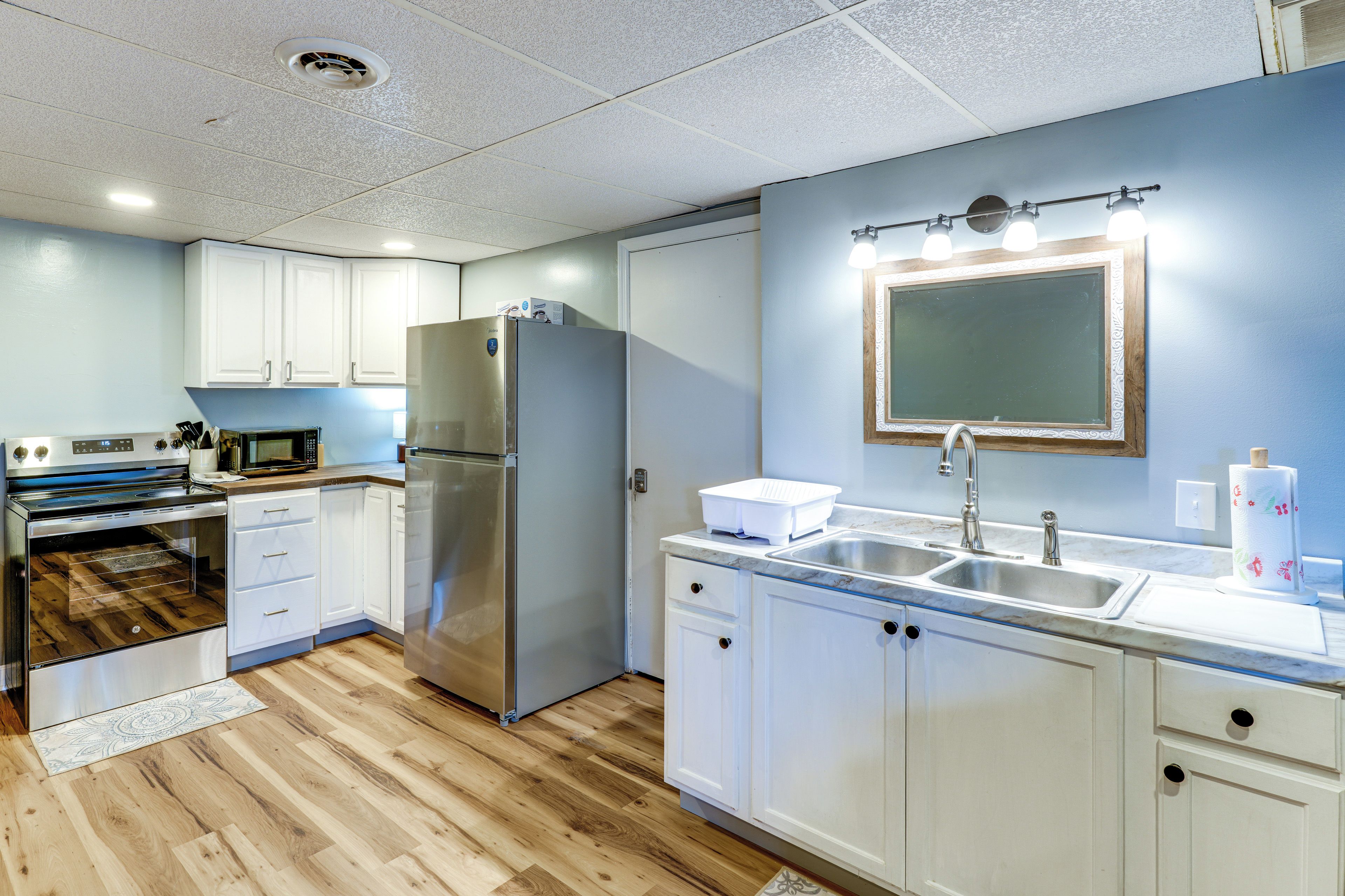 A modern kitchen with white cabinets, stainless steel appliances, a double sink, and a wooden floor.
