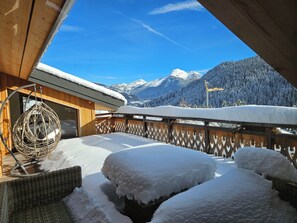 Un balcone imbiancato dalla neve con una sedia in vimini e vista sulle montagne innevate.