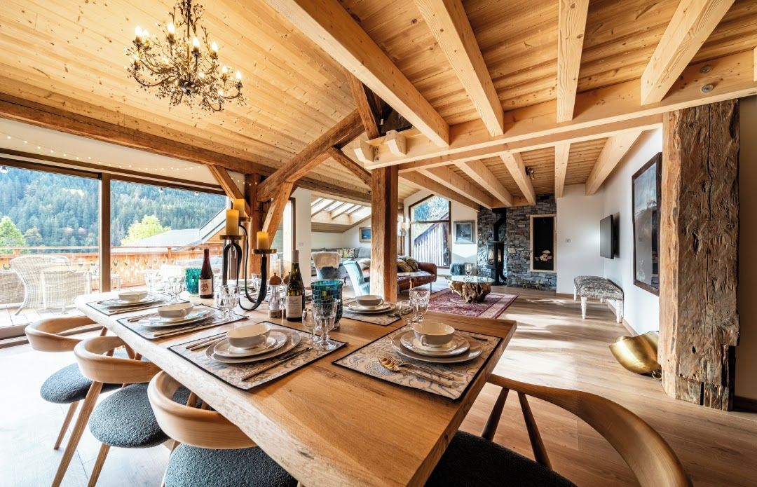 Un coin repas avec une table en bois dressée pour le repas, de grandes fenêtres et un lustre.