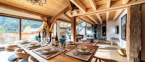 Un coin repas avec une table en bois dressée pour le repas, de grandes fenêtres et un lustre.