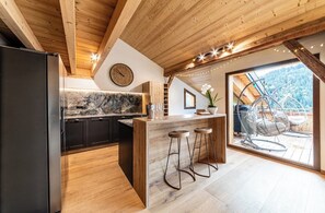 Eine moderne Küche mit Holzboden, einer Marmorarbeitsplatte und einem großen Fenster mit Blick auf einen Balkon und Sitzgelegenheiten im Freien.