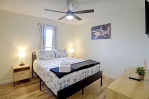 A bedroom with a bed, a ceiling fan, a window with curtains, a bedside table with a lamp, a wall-mounted artwork, and a small plant on a nightstand. - 8 Mi to New Smyrna Beach! Home w/ Poolside Oasis (Edgewater)