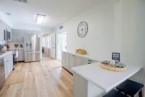 A modern kitchen with stainless steel appliances, a clock on the wall, and a welcome sign.