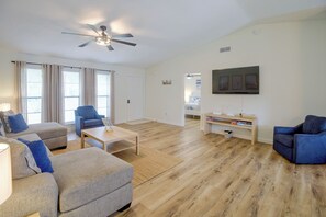 A modern living room with a ceiling fan, a sofa, a coffee table, and a TV mounted on the wall.