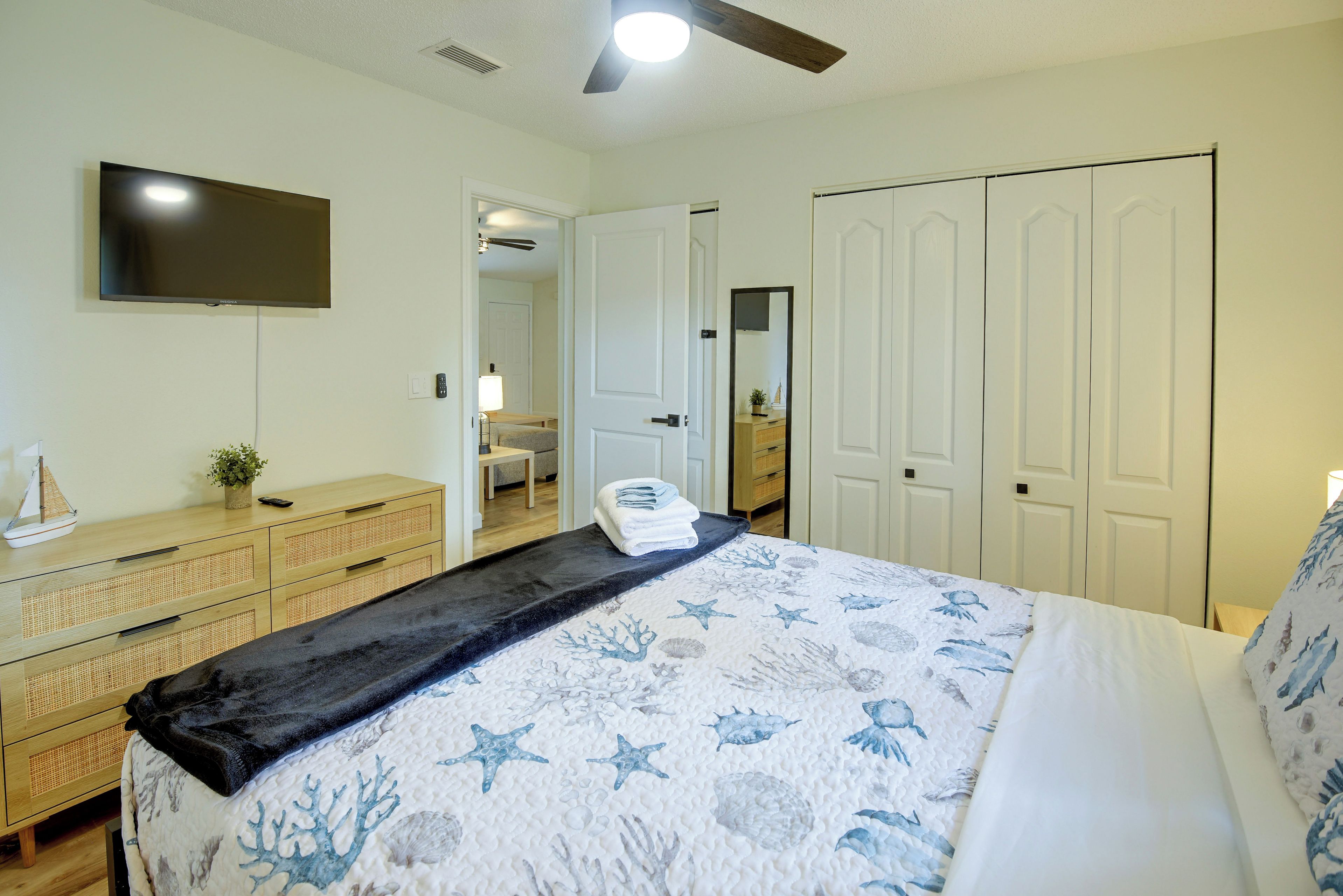 A bedroom with a bed, a TV mounted on the wall, a ceiling fan, and a wardrobe.