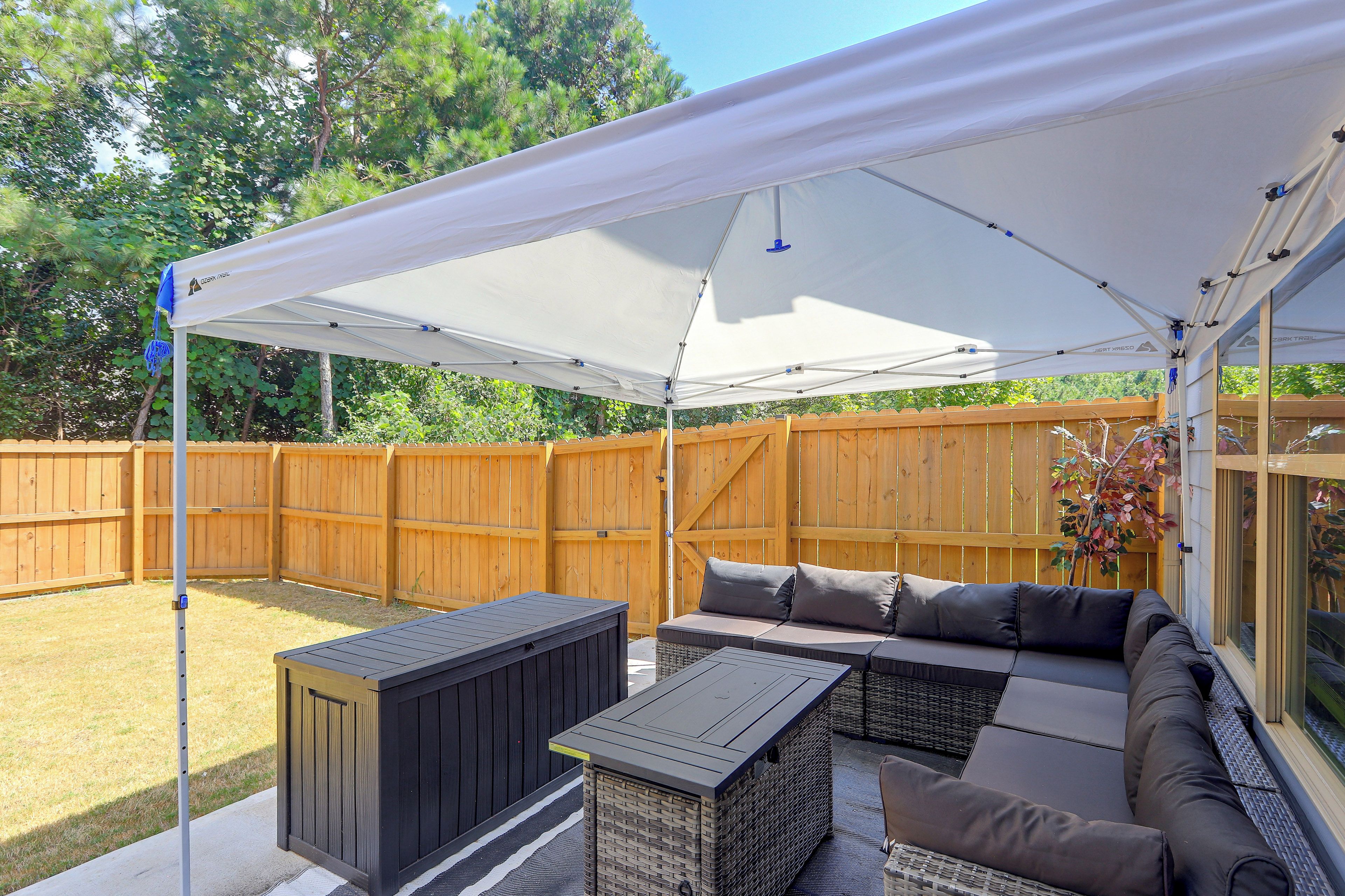 Une terrasse extérieure dotée d’un espace salon couvert, d’une clôture en bois et d’une vue sur le jardin arrière.