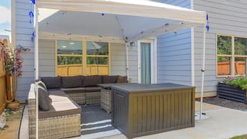 A covered patio area with a sectional sofa, a small table, and a grill.