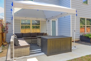 A covered patio area with a sectional sofa, a small table, and a grill.