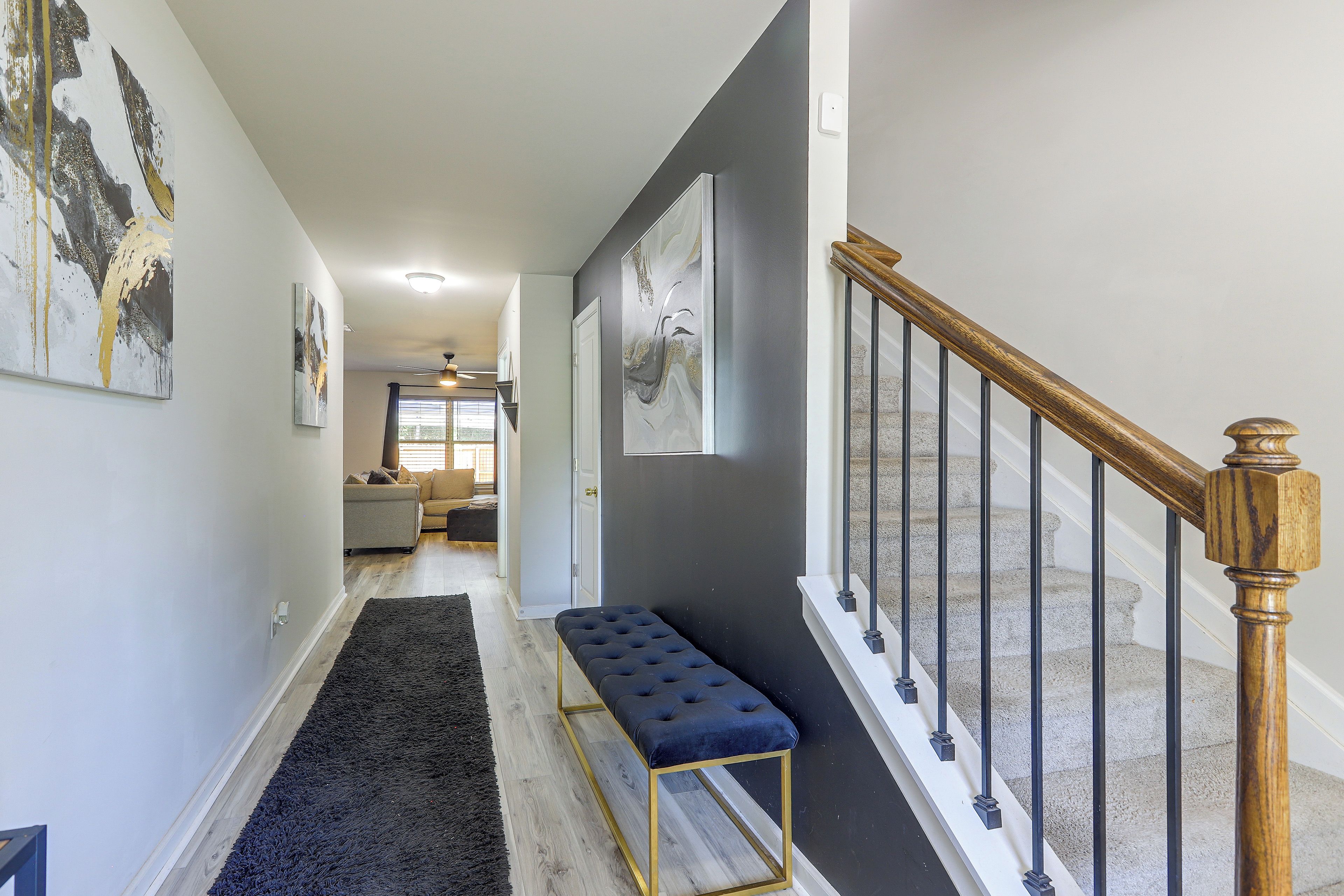 A hallway with a dark blue bench, a staircase with wooden balusters, and artwork on the walls.