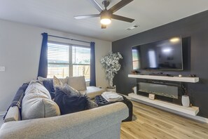 A modern living room with a flat-screen TV, a ceiling fan, and a large window with blinds.