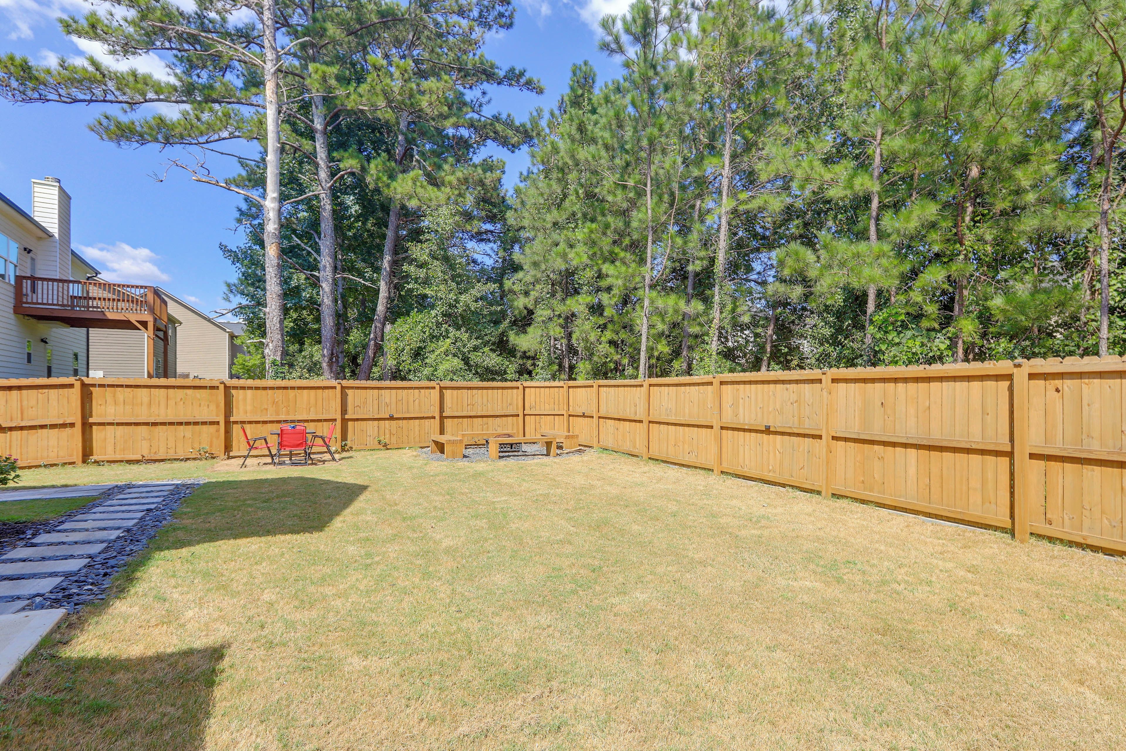A backyard with a wooden fence, a patio area with chairs, and a house in the background.
