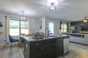 A modern kitchen with a central island, a dining area with blue chairs, and a living space with a sofa.
