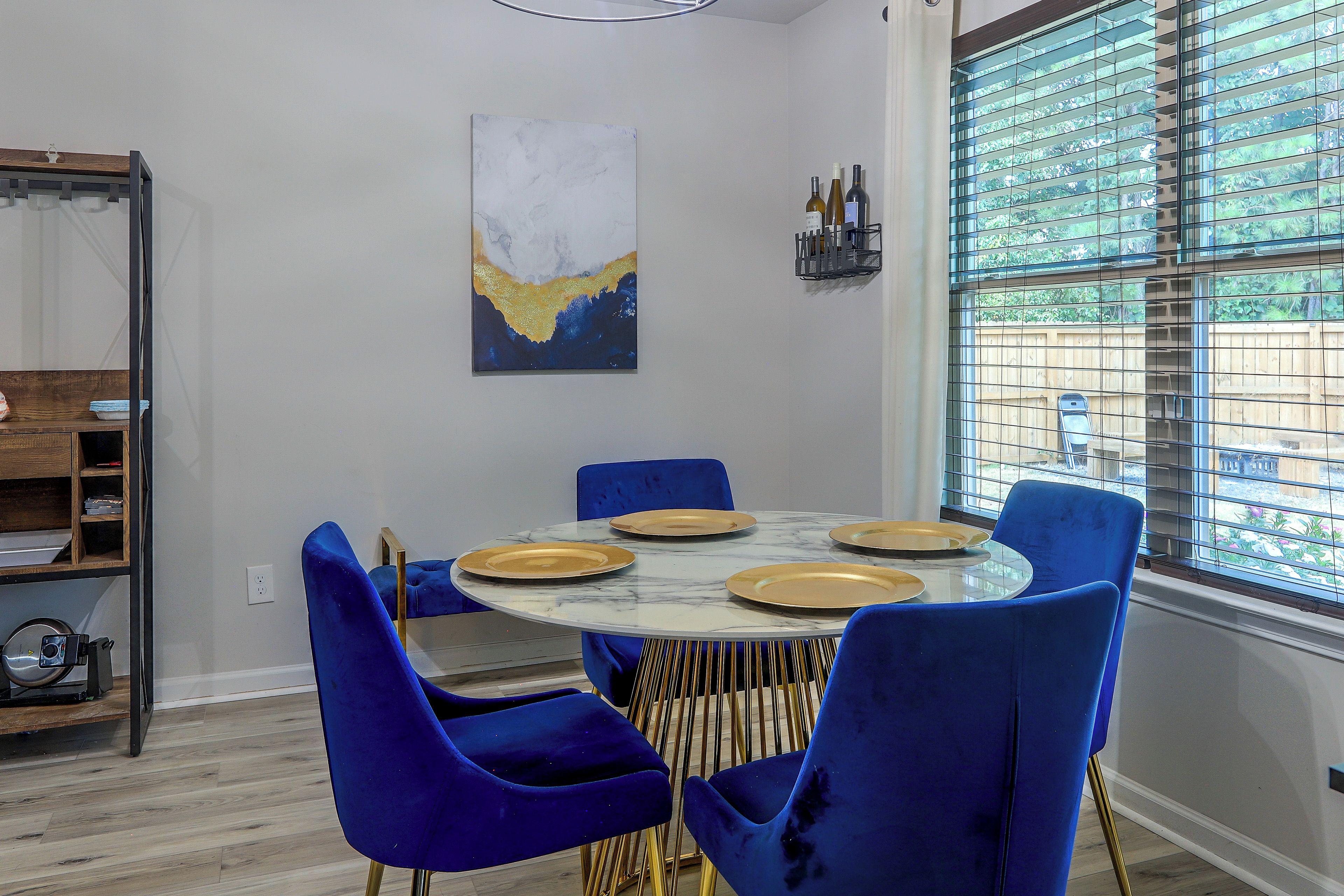 A dining area with a round table, blue chairs, and a painting on the wall.