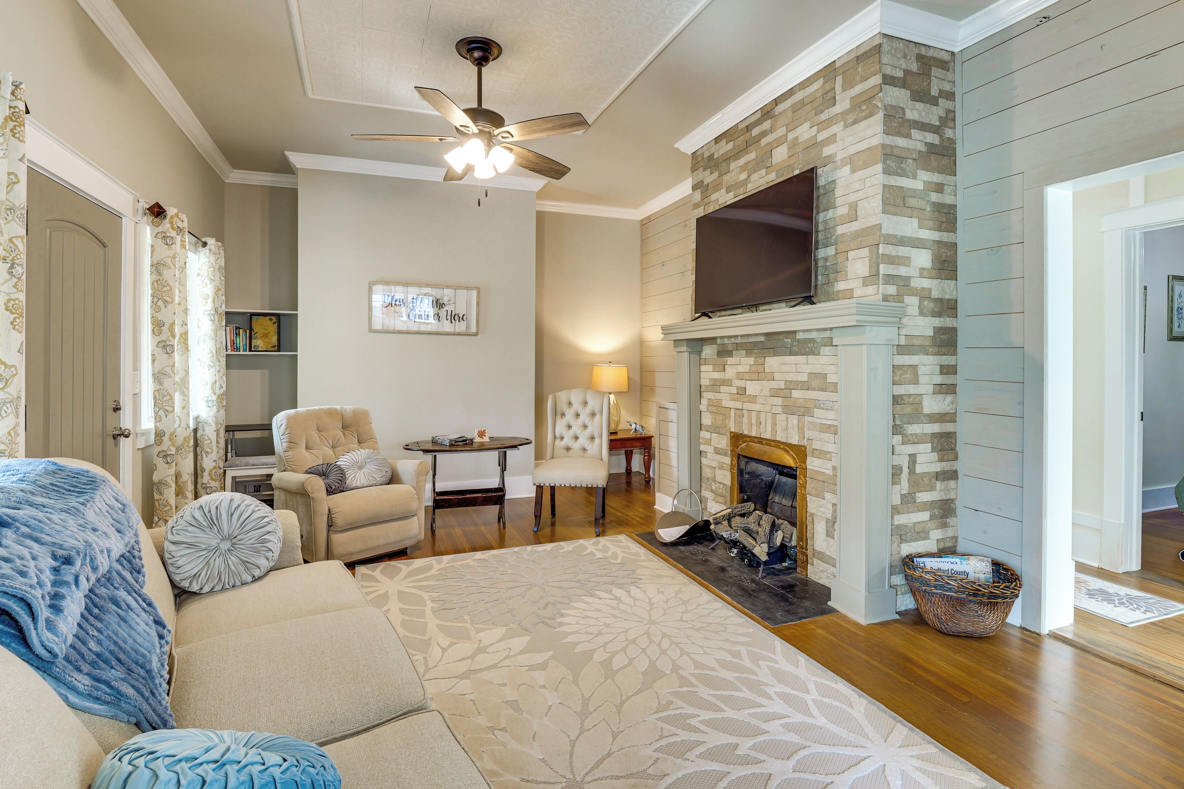 A living room with a fireplace, a ceiling fan, a sofa, and a television mounted on the wall.